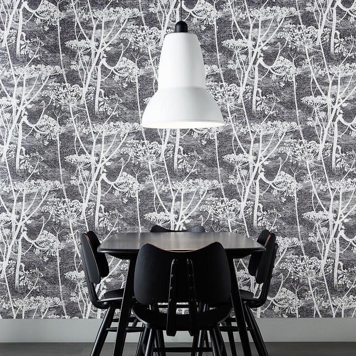 Weiße Anglepoise Original 1227 Giant Pendelleuchte über schwarzem Esstisch mit Stühlen vor gemusterter Tapete.