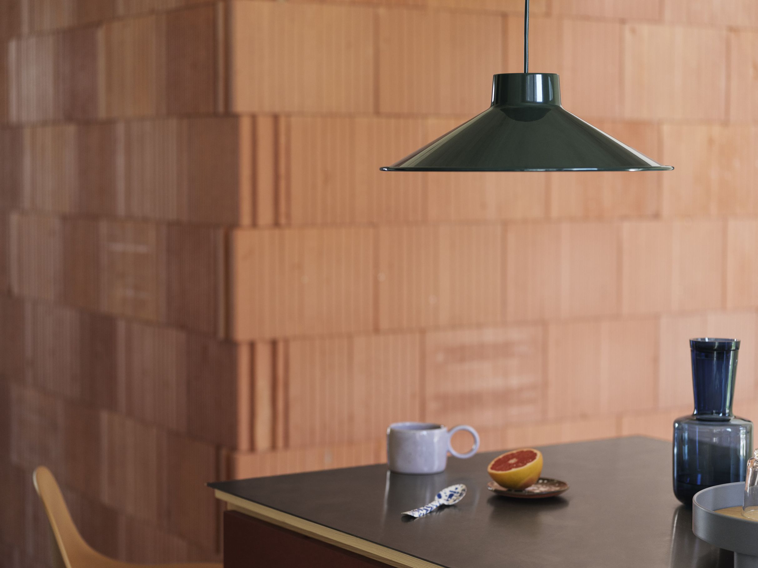 Grüne Muuto Top Pendant Pendelleuchte über Esstisch mit Tasse, Grapefruit und blauer Karaffe.