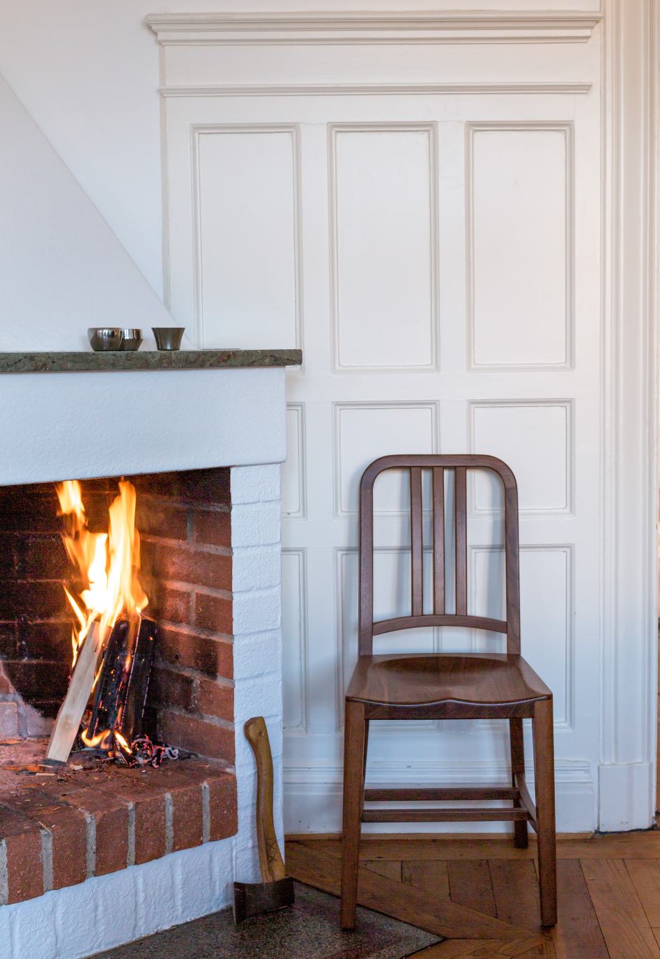 Walnussfarbener Holzstuhl der Marke Emeco neben einem Kamin mit brennendem Feuer.