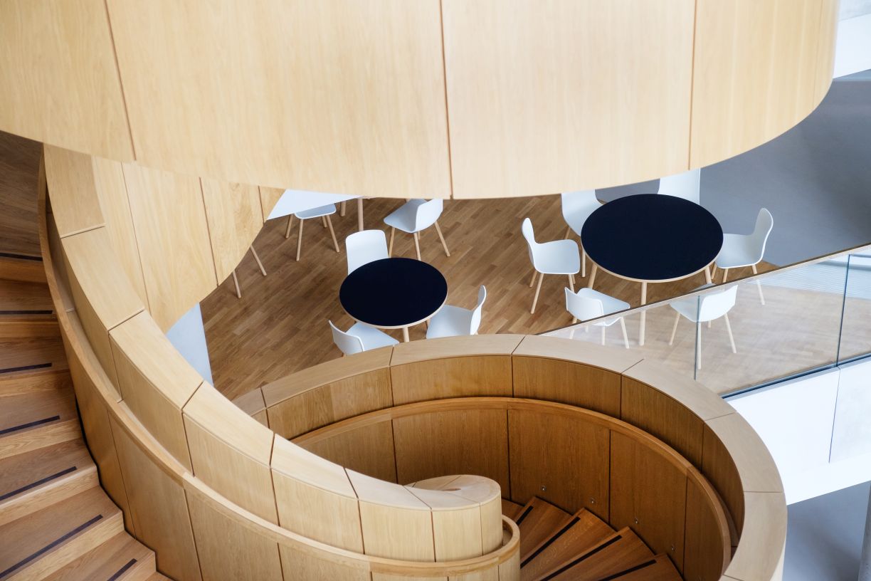 Draufsicht auf eine Wendeltreppe mit weißen Vitra Hal RE Wood Stühlen und runden Tischen.