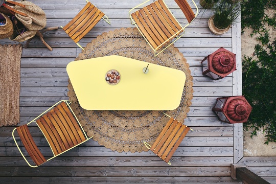 Draufsicht: Gelber Tisch mit Teakholz Stühlen von Fermob auf einer Holzterrasse.