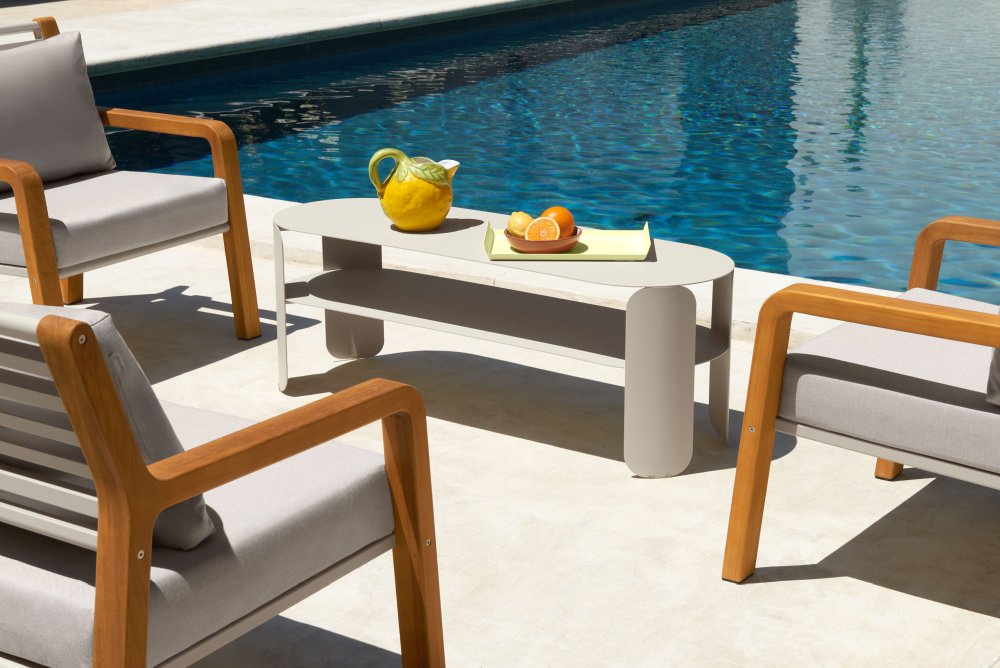 Fermob Somerset Sessel und Couchtisch im Außenbereich neben einem Pool, modernes Gartenmöbel-Set mit Holzarmlehnen.