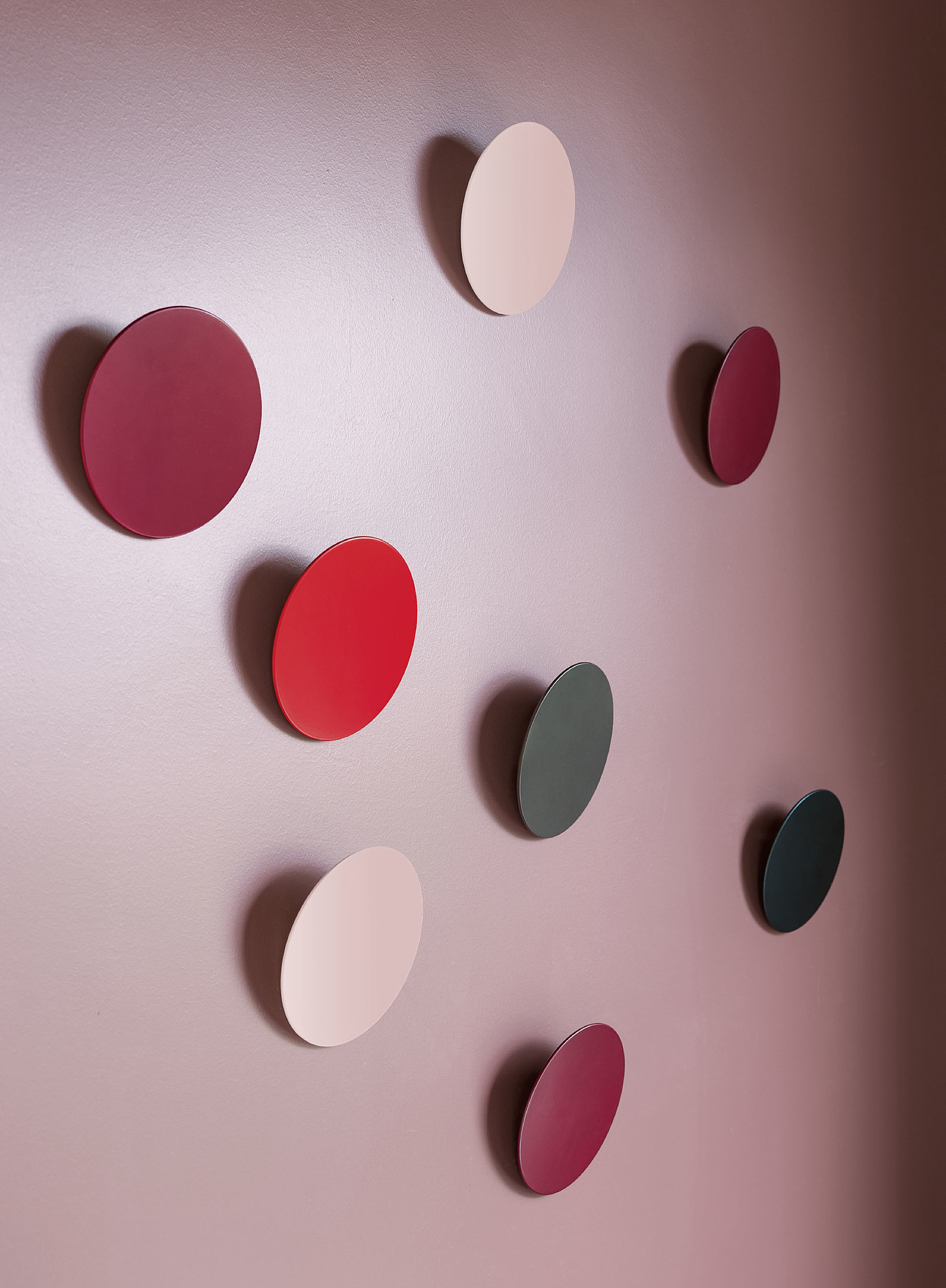 Mehrere Schönbuch Disk Wandhaken in verschiedenen Farben an einer rosa Wand.