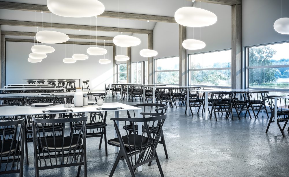 Helle, moderne Kantine mit Tischen und Stühlen, beleuchtet durch mehrere weiße Avion Pendelleuchten von Fritz Hansen.