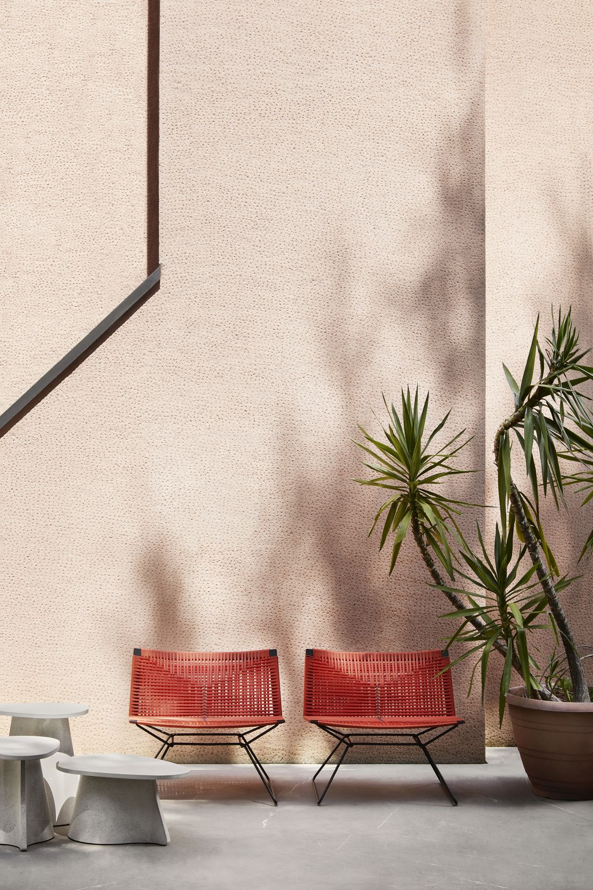 Fossil Beistelltisch von MDF Italia neben zwei roten Outdoor-Stühlen und einer Topfpflanze.