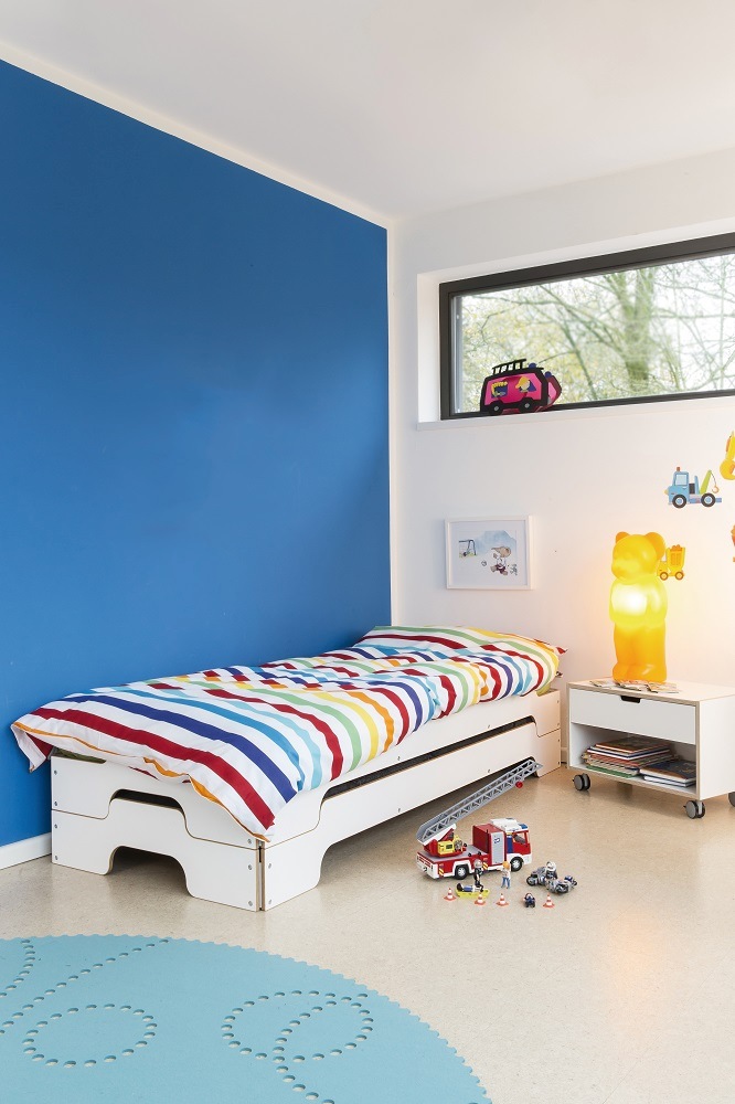 Kinderzimmer mit weißem Bett und Müller Möbelwerkstätten Nachttisch, Gummibärchen Lampe und Spielzeug.
