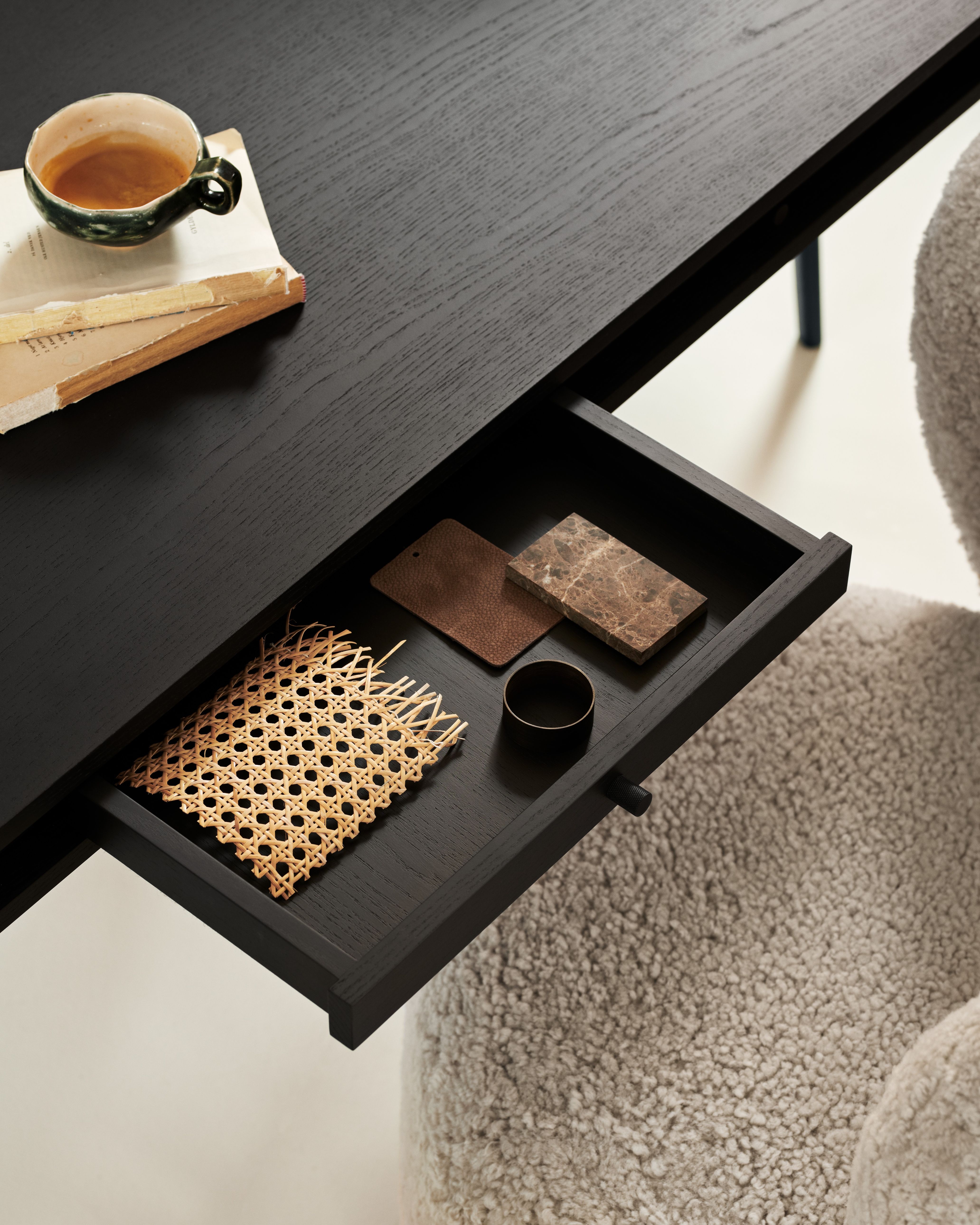 Detailaufnahme des JFK Büroschreibtischs von Norr11 mit offener Schublade, Materialproben und Kaffeetasse auf einem Buch.