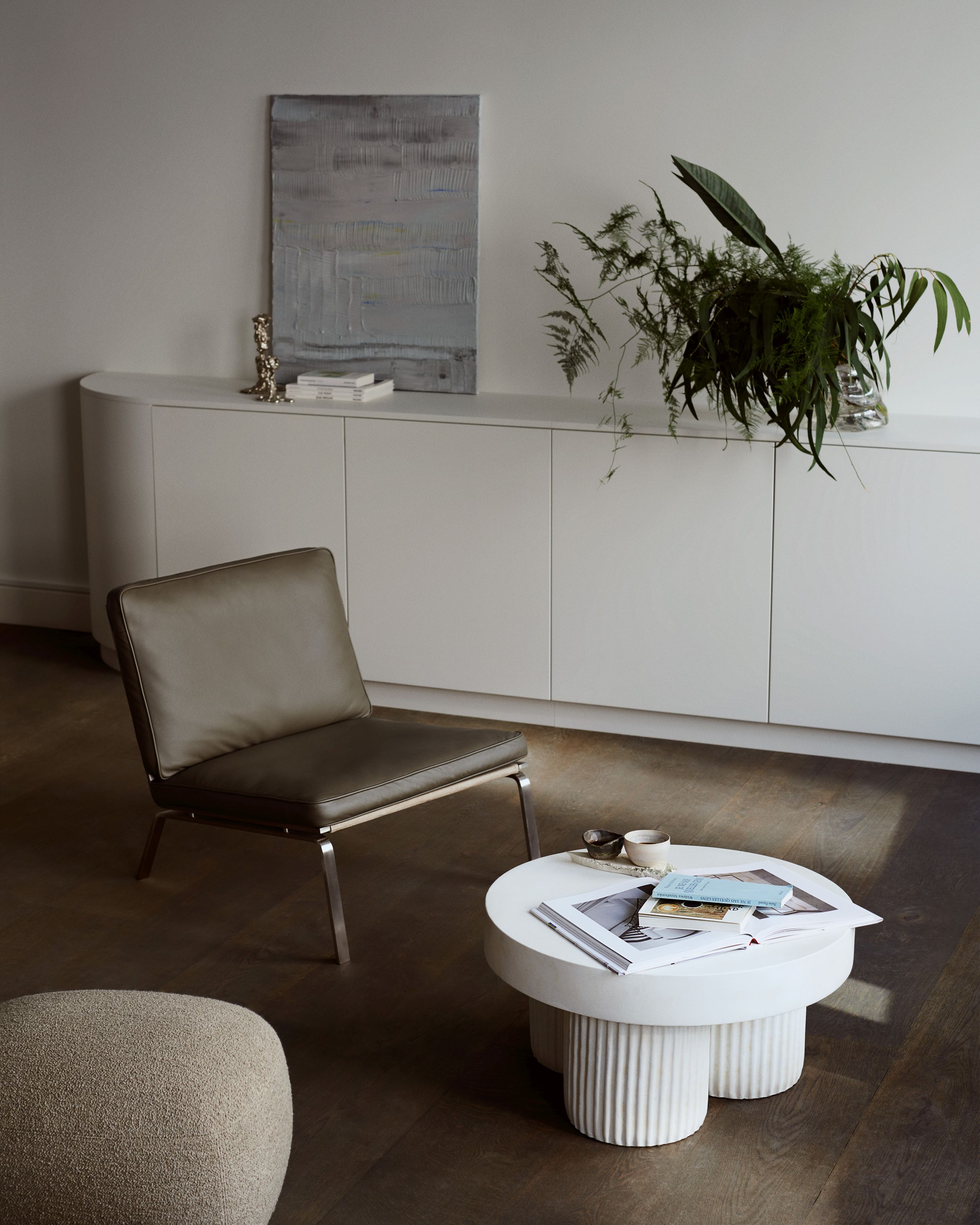 Wohnzimmer-Szene mit Liége Pouf Barnum Bouclé, Sessel und weißem Couchtisch auf dunklem Holzboden.