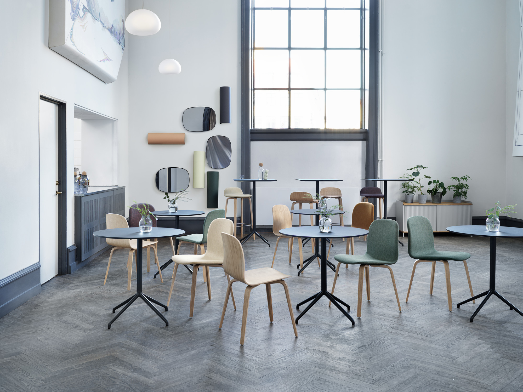 Innenraumansicht mit mehreren Muuto Visu Stühlen mit Holzgestell an kleinen Tischen in einem hellen Raum.