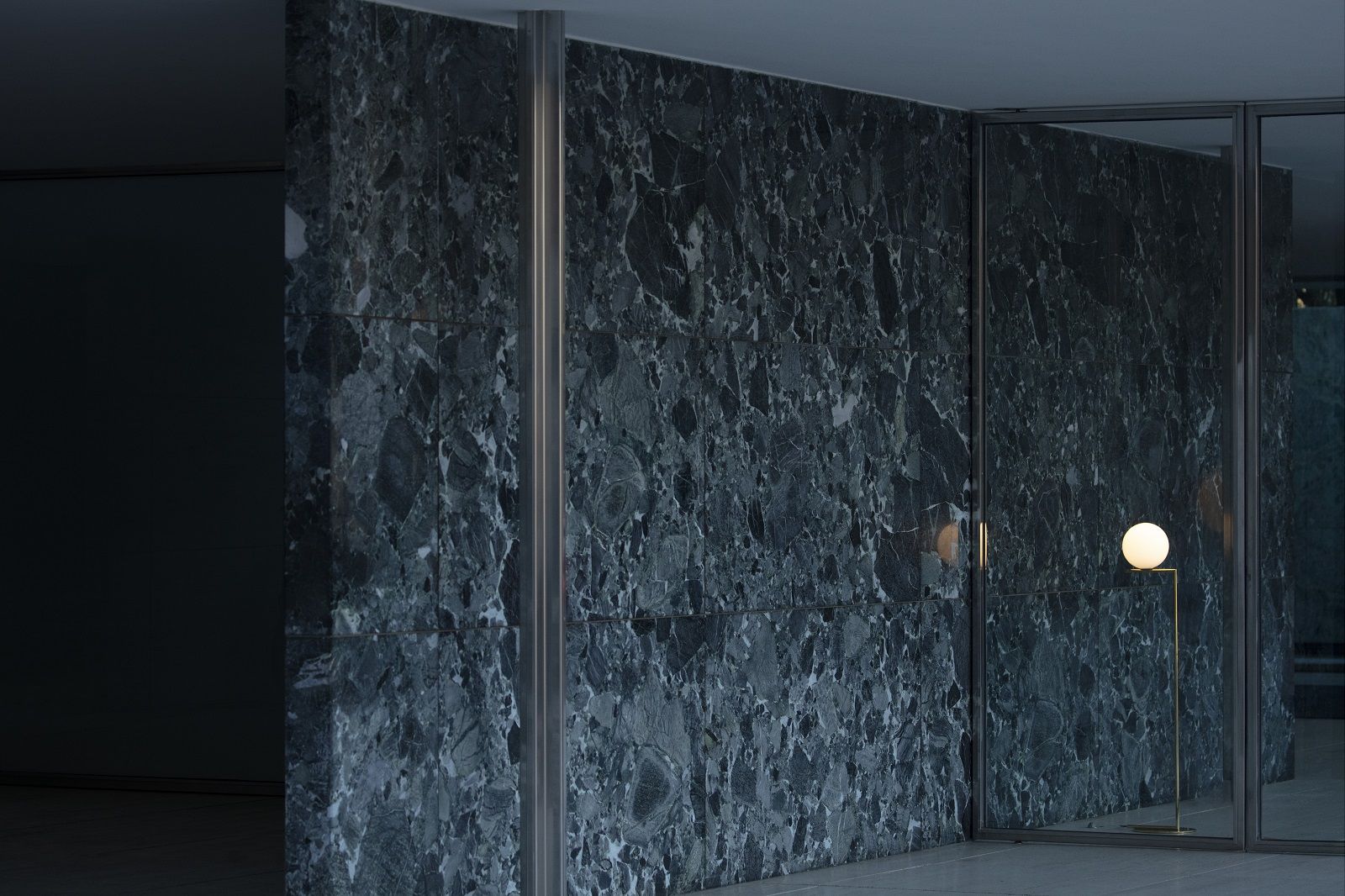 IC F1 Stehleuchte von Flos in Gold vor einer dunklen Marmorwand.