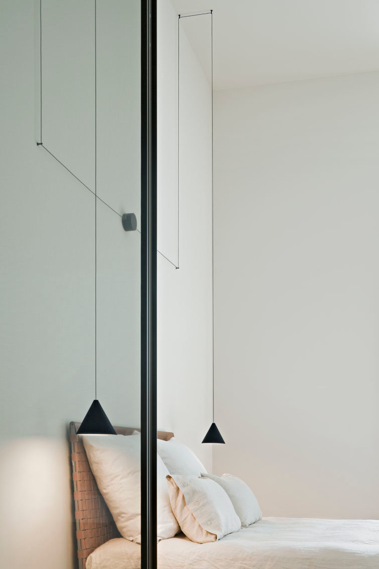 Schwarze Flos String Light Cone Pendelleuchte über Bett, minimalistisches Design für Schlafzimmerbeleuchtung.