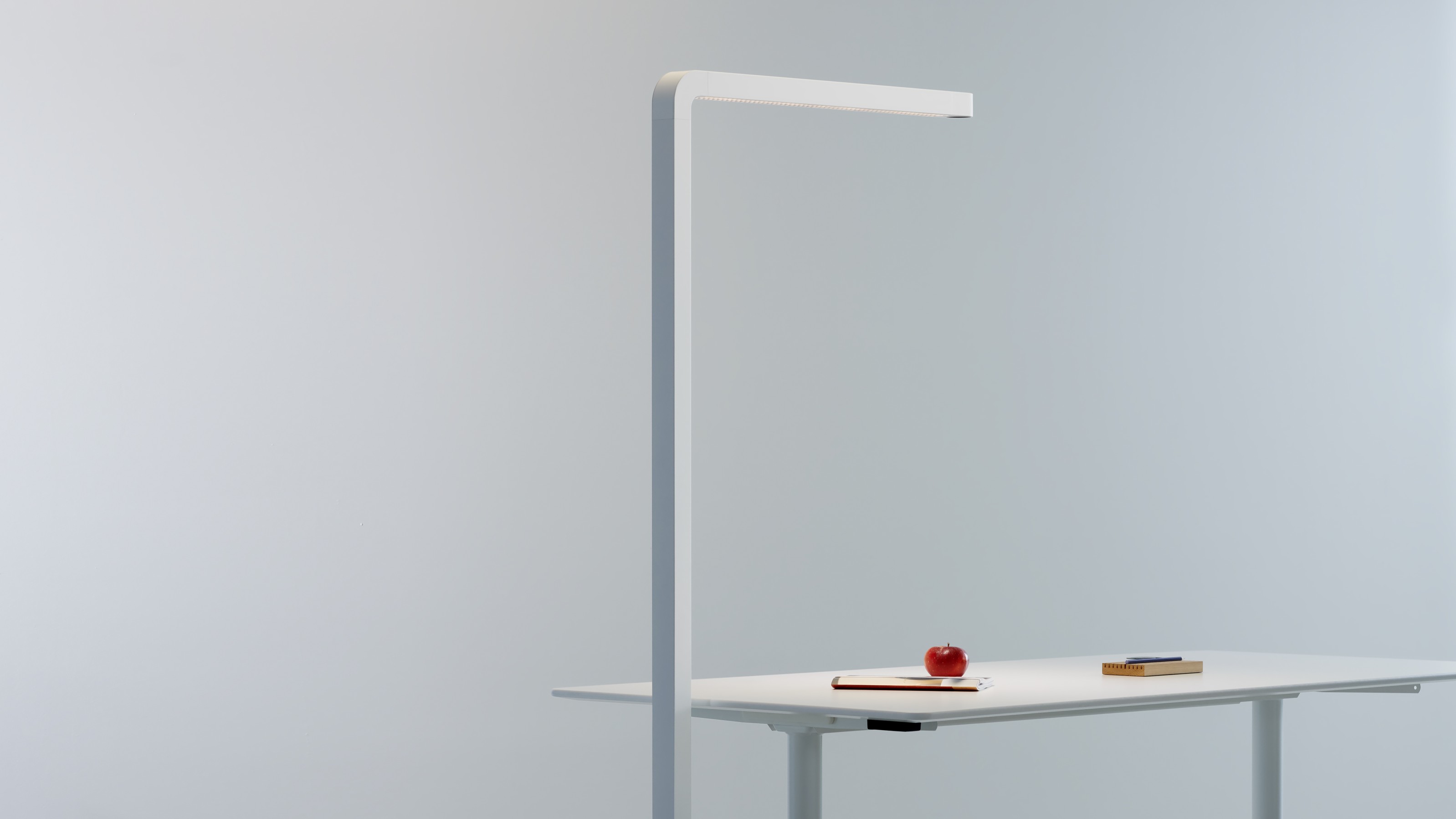 Team Agile Stehleuchte in Grau über einem Schreibtisch mit Apfel, Notizbuch und Stifthalter.