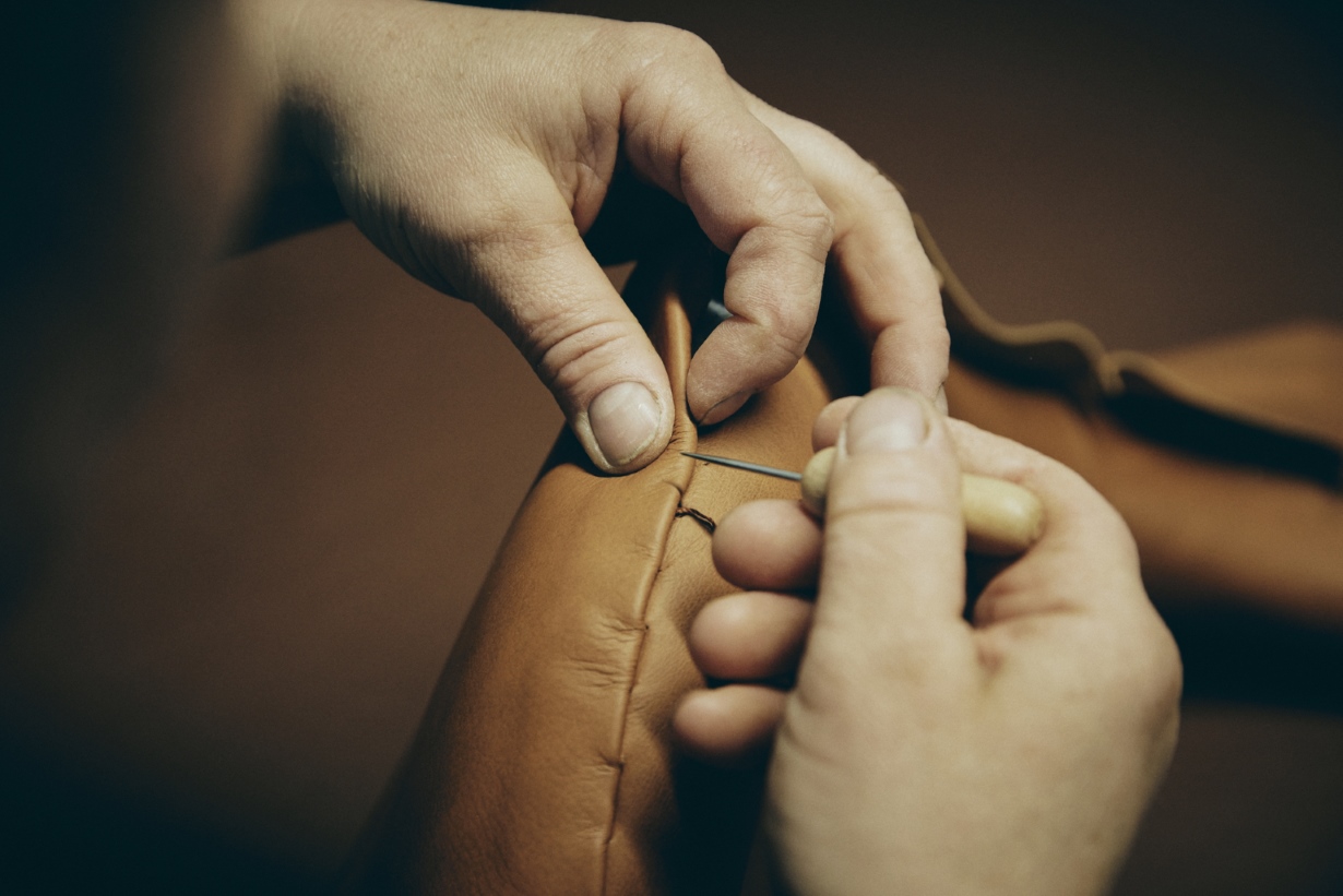 Handgefertigte Ledertasche: Detailaufnahme der Handnaht mit Nadel und Faden für hochwertige Lederwaren.