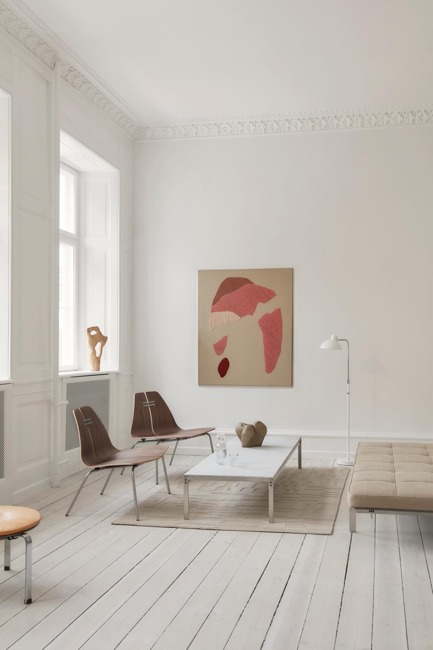 Heller Wohnraum mit zwei PK23 Loungesesseln von Fritz Hansen, Couchtisch, Teppich und Kunstwerk an der Wand.