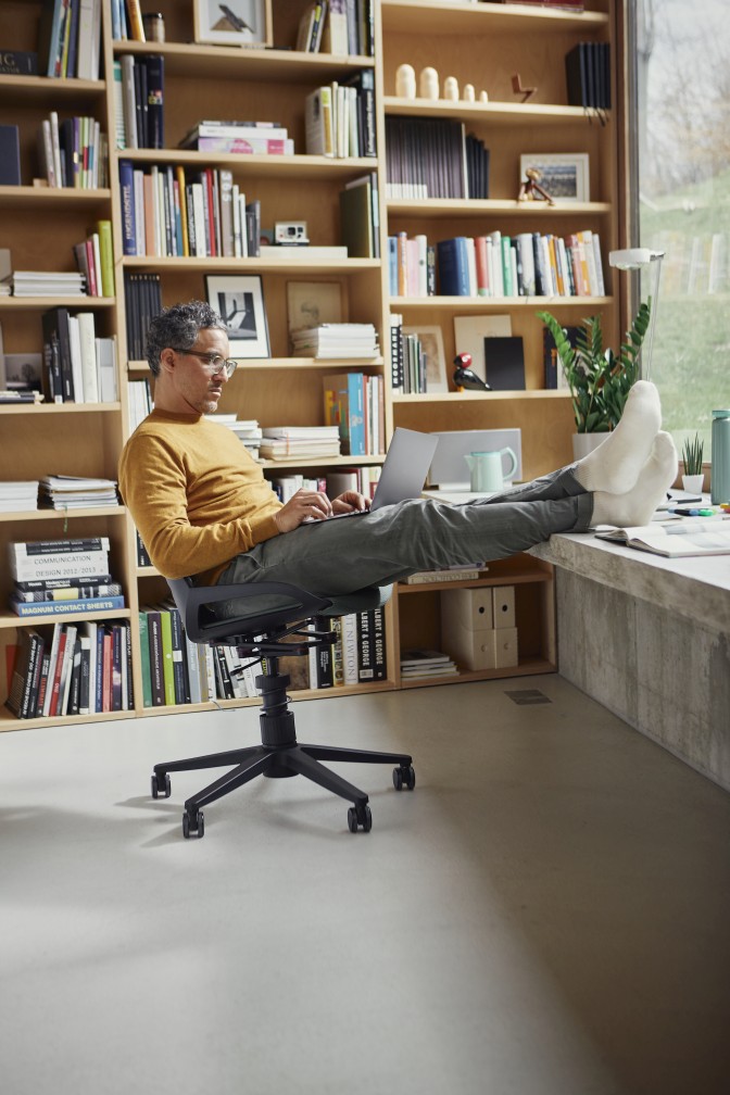 Mann sitzt entspannt mit Laptop auf dem Numo Bürodrehstuhl mit Rollen von Aeris.