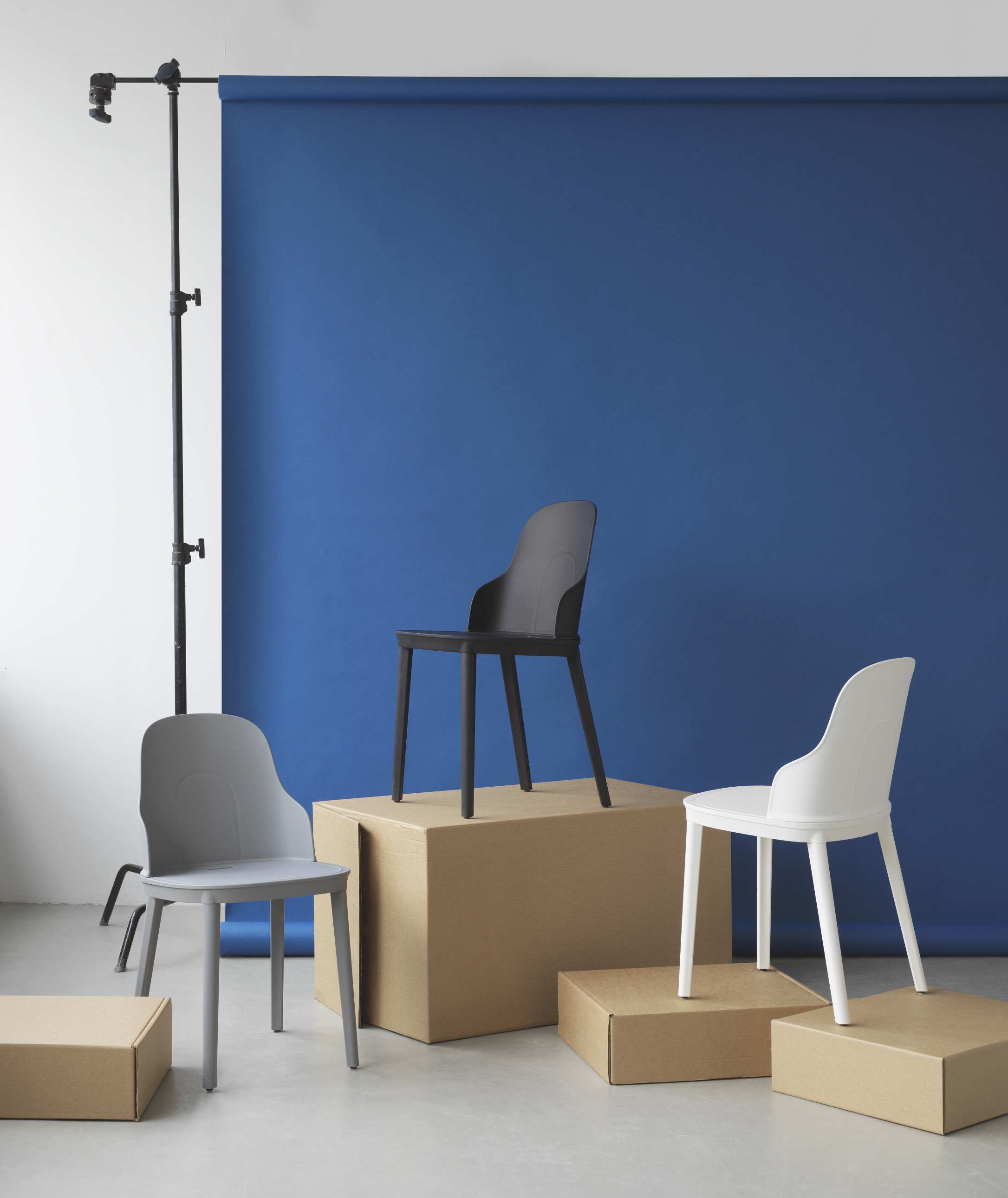 Allez Chair von Normann Copenhagen in Weiß, Grau und Schwarz auf Kartons vor blauem Hintergrund.