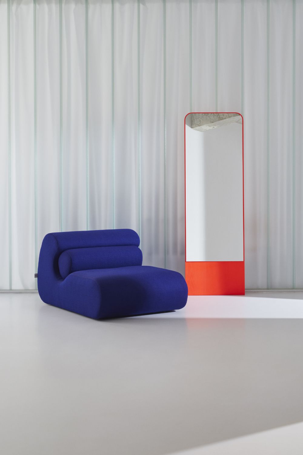 Blauer OLA Sofa Pouf OUT aus Stoff neben einem orangefarbenen Spiegel in minimalistischem Interieur.