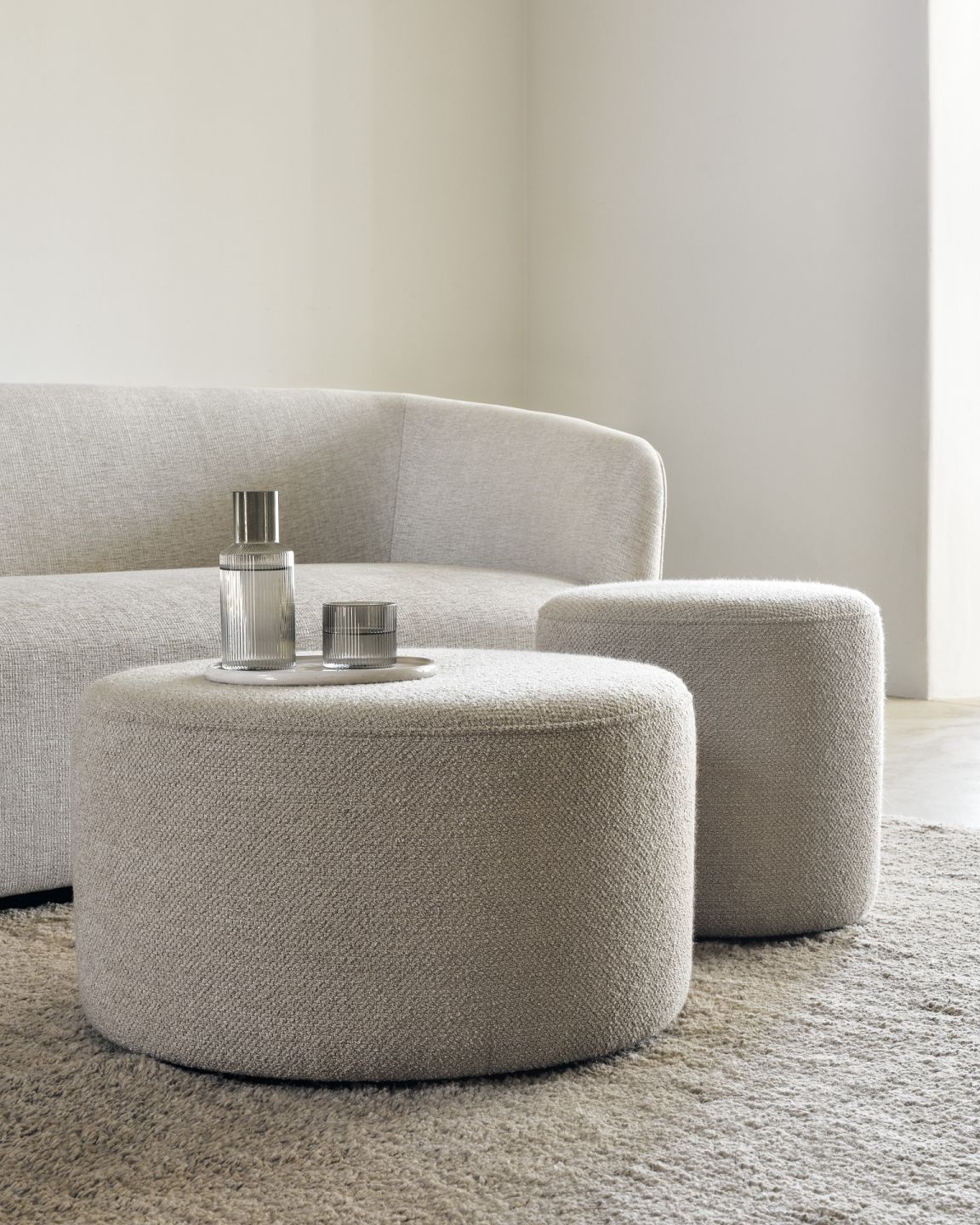 Beige Poufs und Sofa im Wohnzimmer, runder Hocker als Couchtisch mit Wasserflasche und Glas.