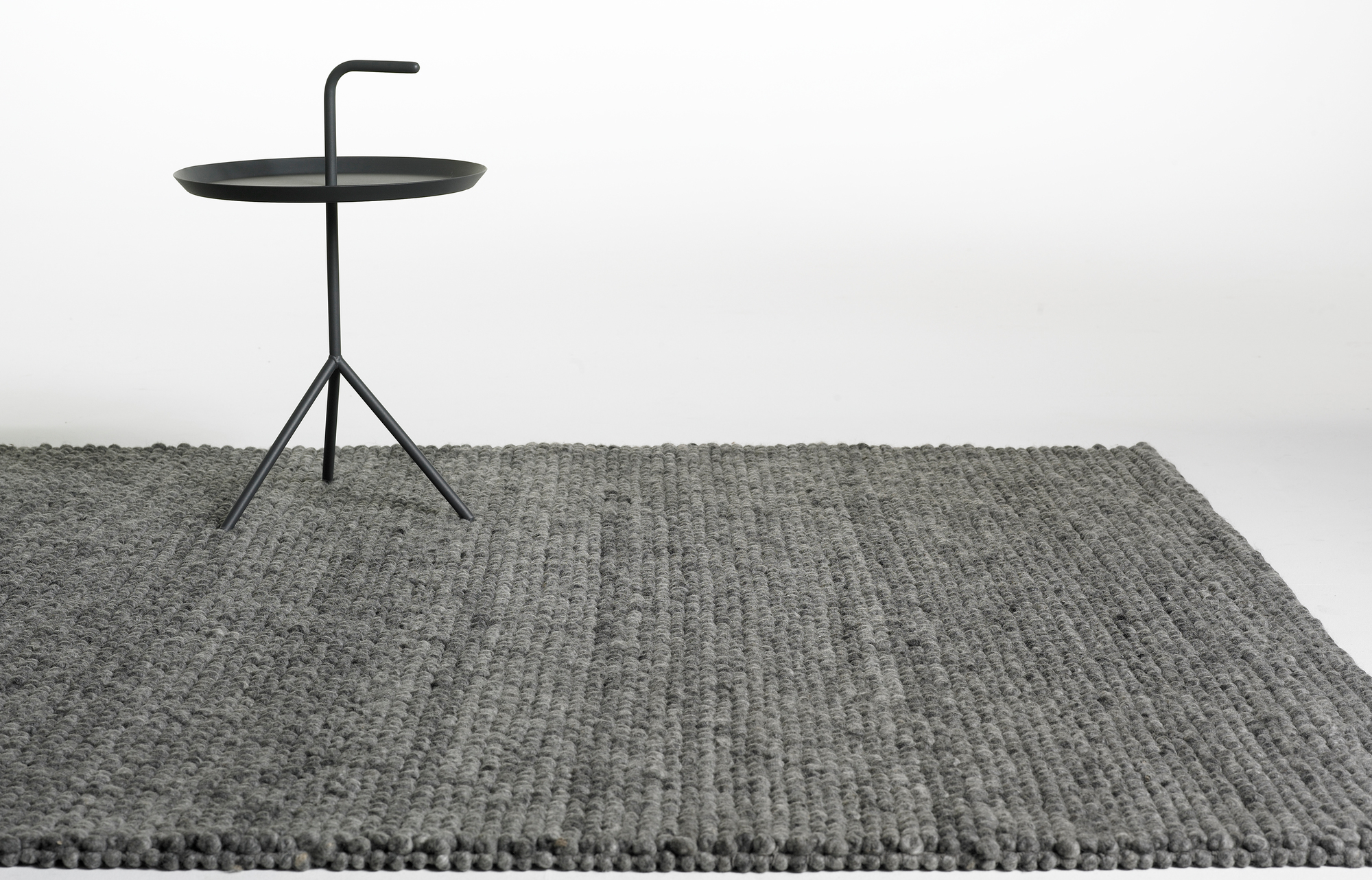 Grauer Hay Peas Teppich (140x80 cm) aus Wolle, mit kleinem, schwarzen Beistelltisch.