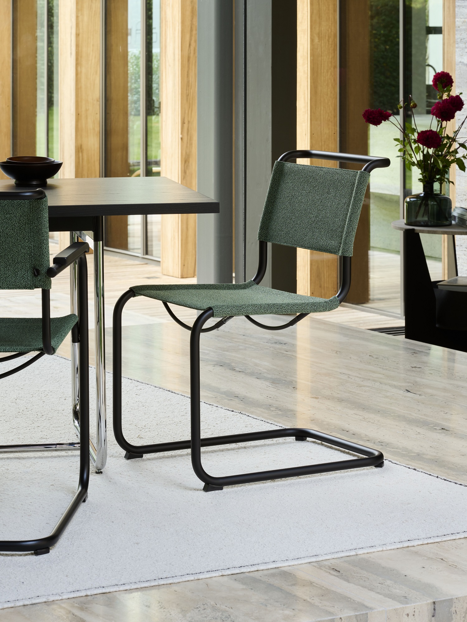 Nahaufnahme eines grünen Thonet S 33 Freischwinger Stuhls mit schwarzem Stahlrohrgestell im modernen Esszimmer.