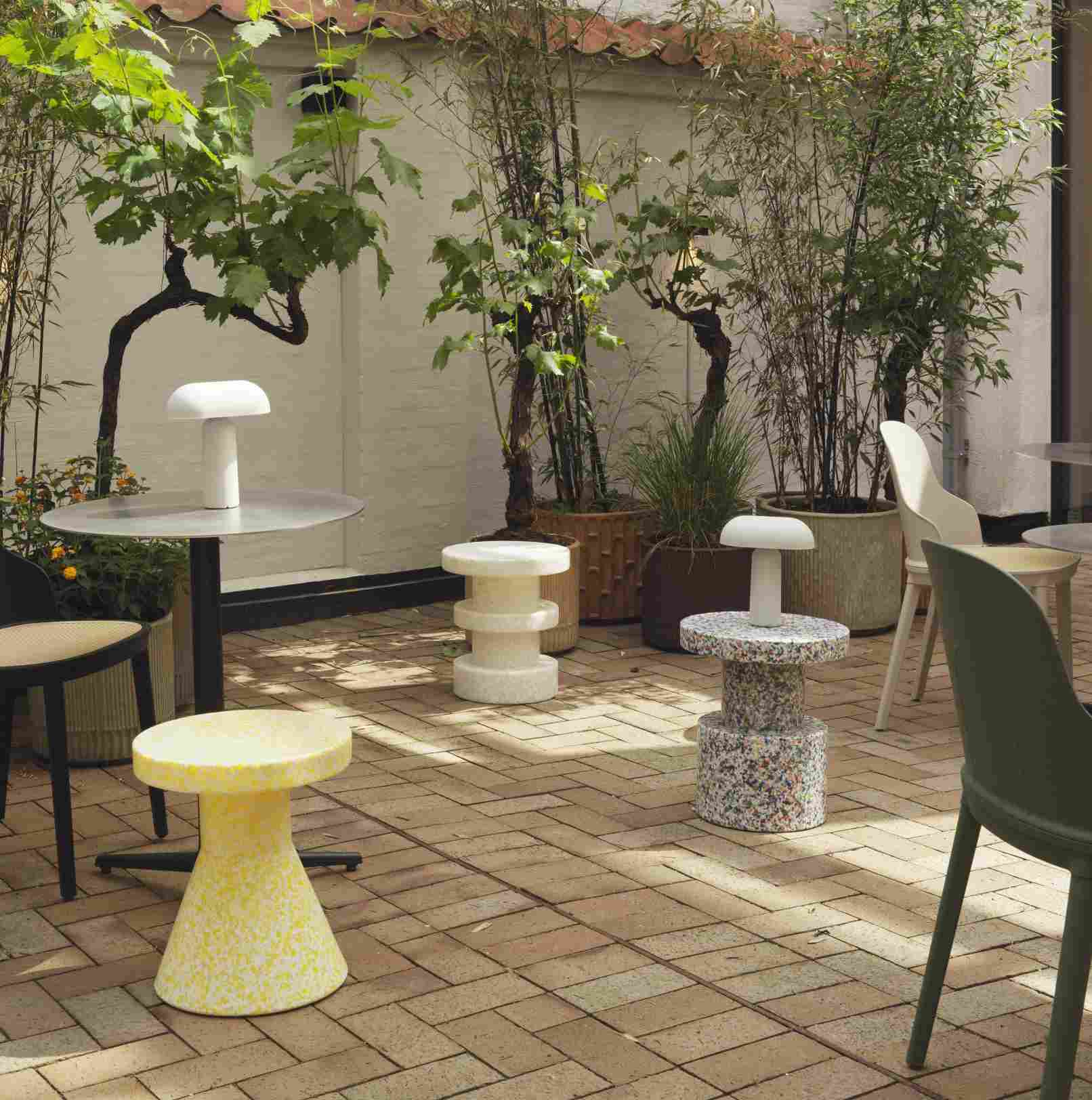 Gelber Bit Stool Cone Hocker von Normann Copenhagen im Außenbereich mit Pflanzen und Tischen.