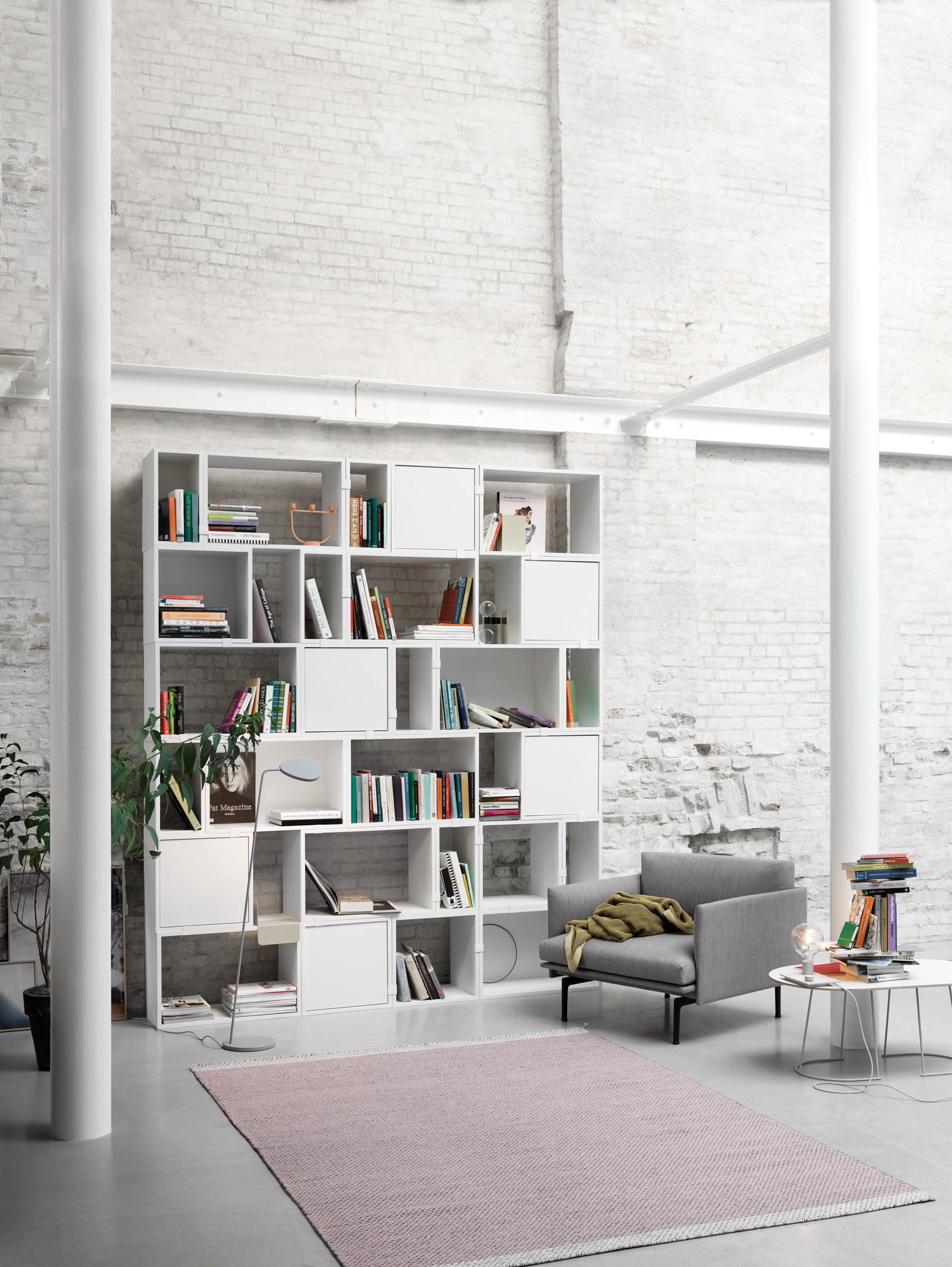 Grauer Muuto Outline Chair Sessel in modernem Wohnzimmer mit Bücherregal und Teppich.