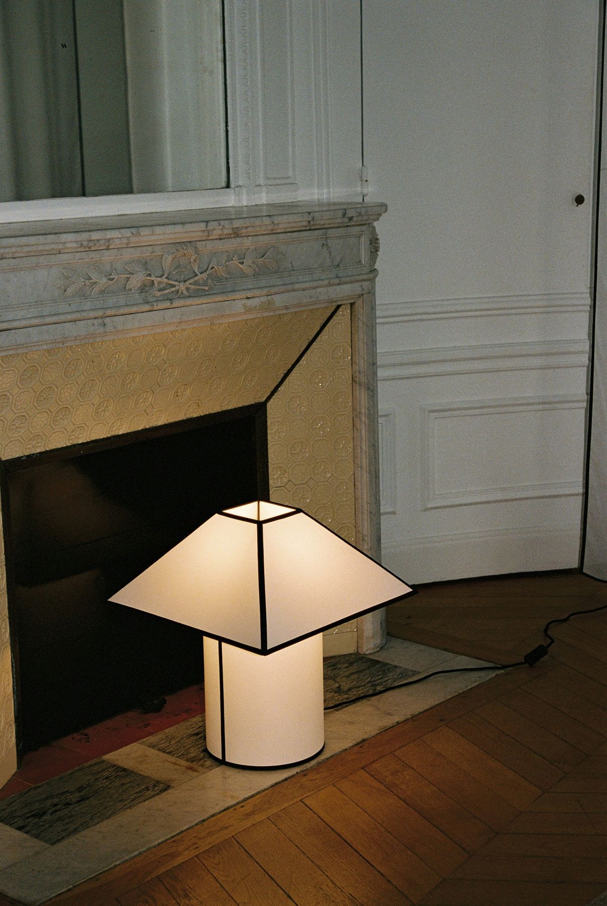 Ava Pyramid Table Lamp von Hay, moderne Tischleuchte mit geometrischem Schirm, neben einem Kamin.
