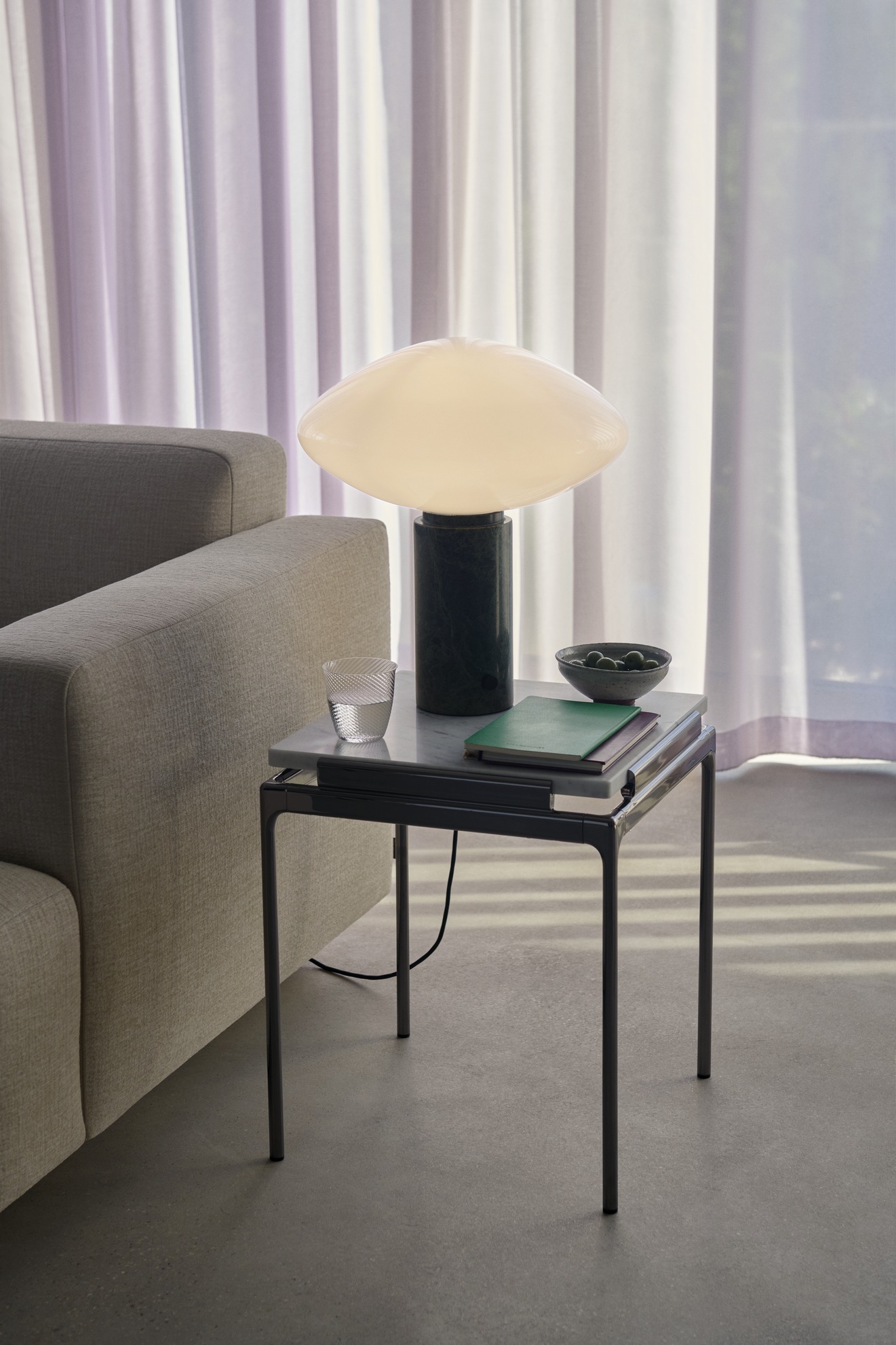 AndTradition Sett LN11 Beistelltisch: Marmor Tischplatte mit Lampe, Glas und Schale neben einem Sofa.