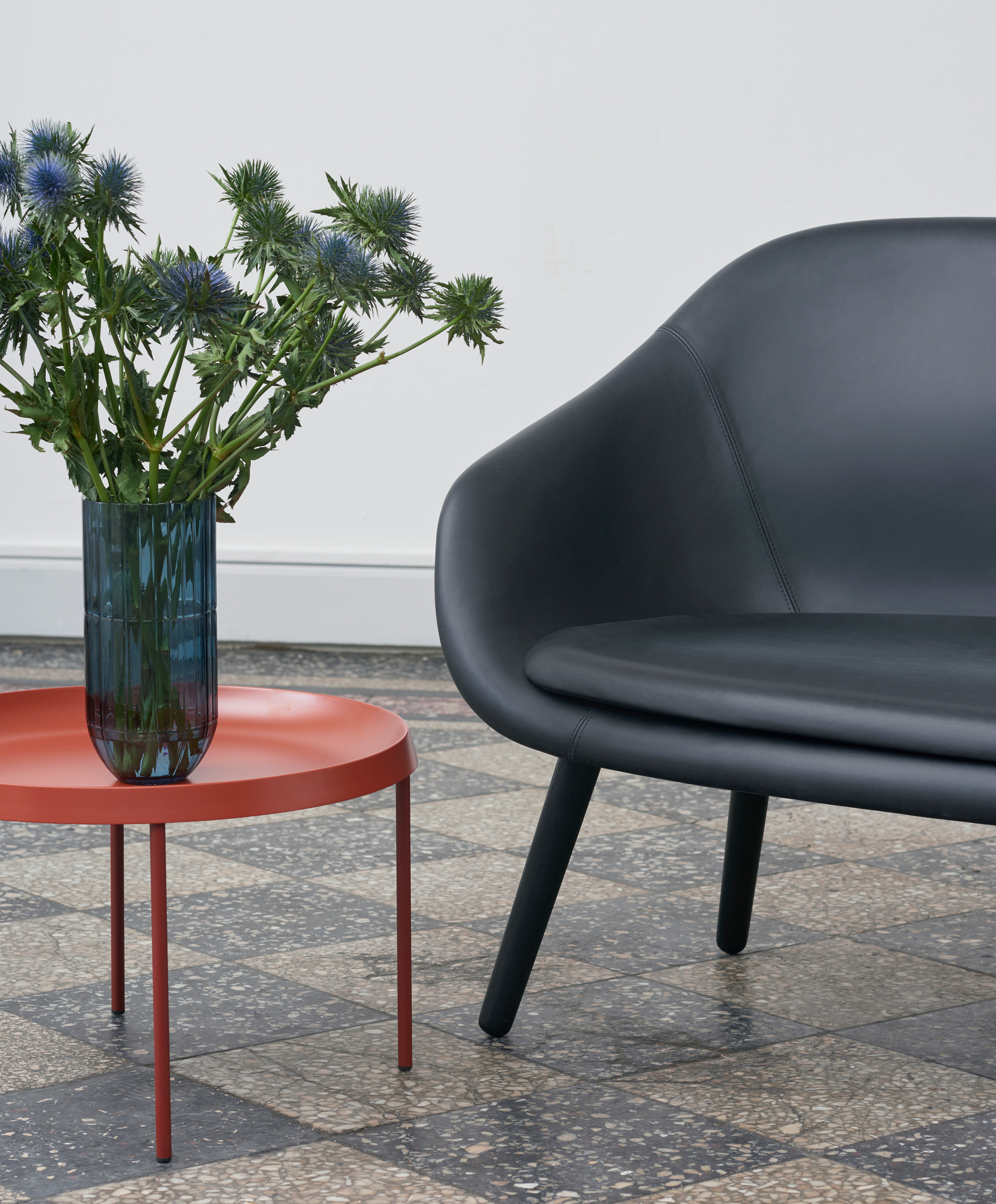 Schwarzes About a Lounge Sofa von Hay neben einem roten Beistelltisch mit blauer Blumenvase.