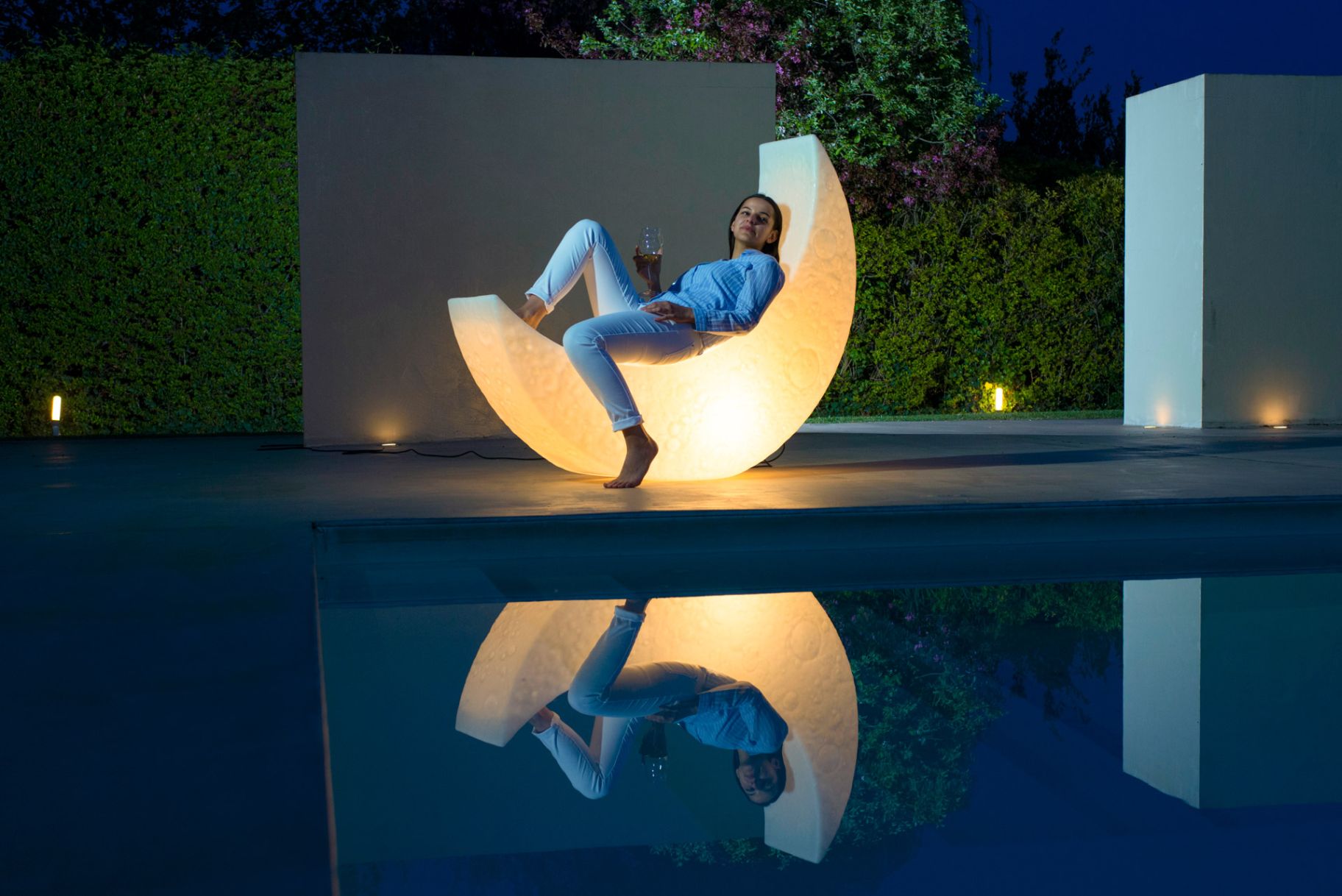 Frau entspannt in der leuchtenden My Moon Lampe von Seletti am Pool mit Spiegelung im Wasser.