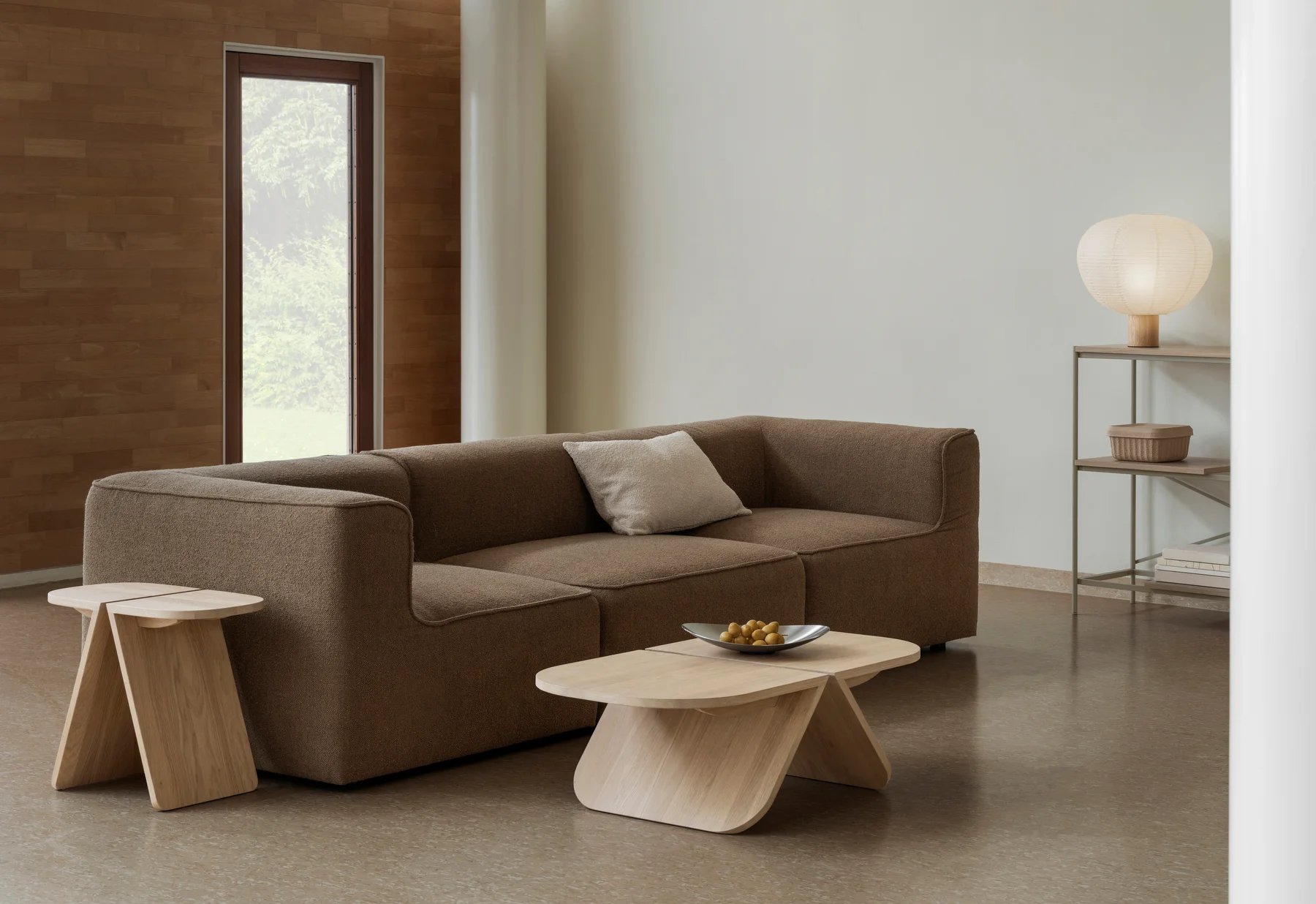 Wohnzimmer-Szene mit braunem Sofa, Holztischen und Blomus Kami Reispapier Tischleuchte auf einem Regal.