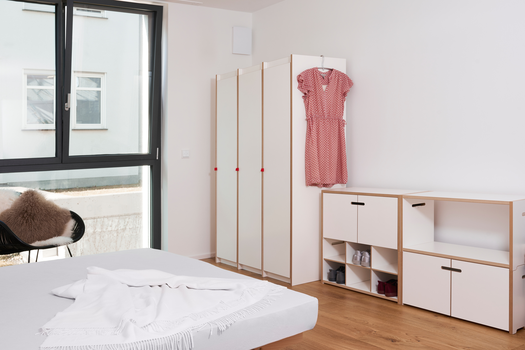 Helles Schlafzimmer mit Tojo Hochstapler Regal Anbaumodul, Kleiderschrank, Bett und Stuhl für moderne Einrichtung.