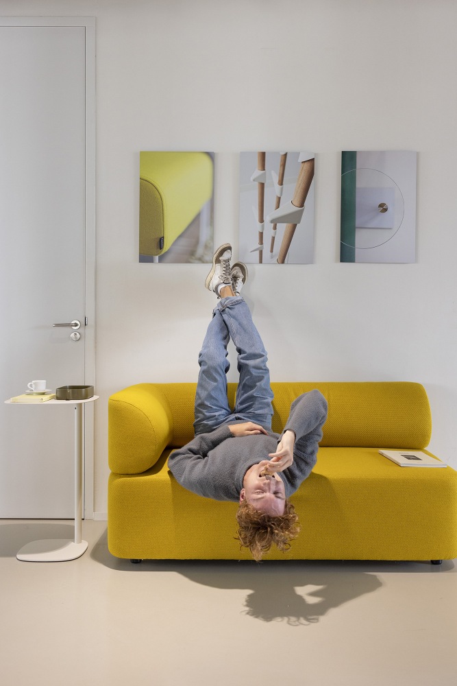 Mann liegt entspannt auf gelbem Mezza Sitzelement Sofa von Cascando, Füße an der Wand.