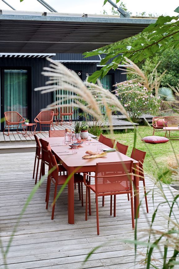 Cadiz Armlehnenstuhl von Fermob in Terrakotta an Esstisch im Garten auf Holzterrasse.