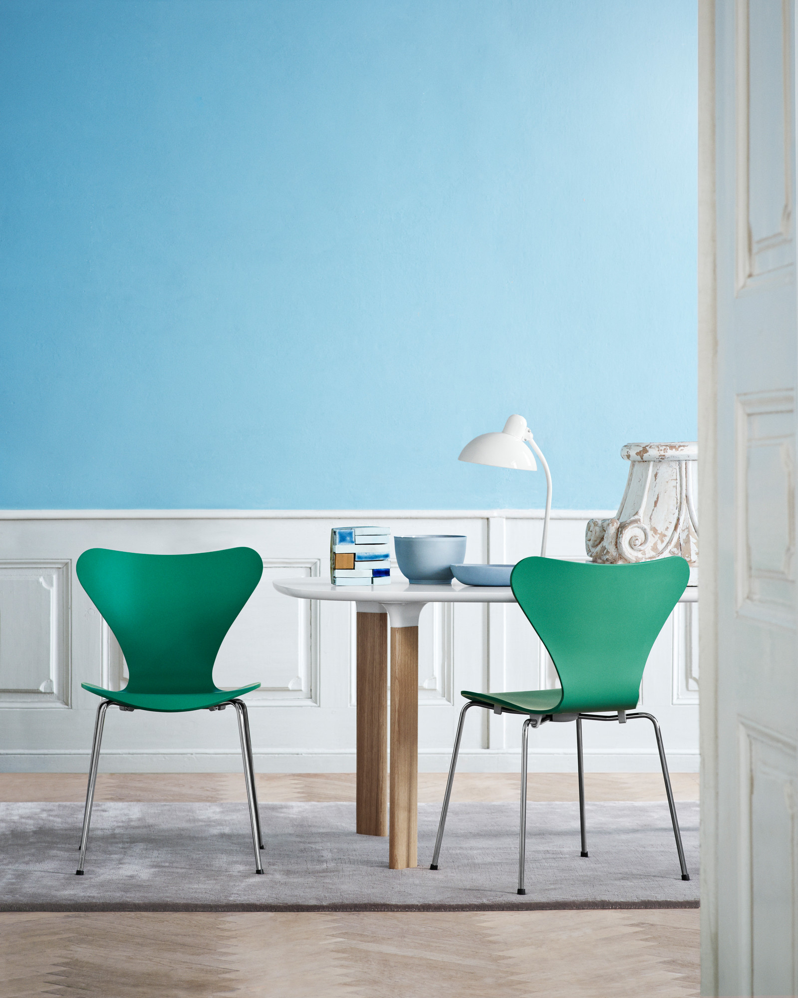 Helle Szene mit KAISER idell 6556 T Tischleuchte und grünen Stühlen von Fritz Hansen.