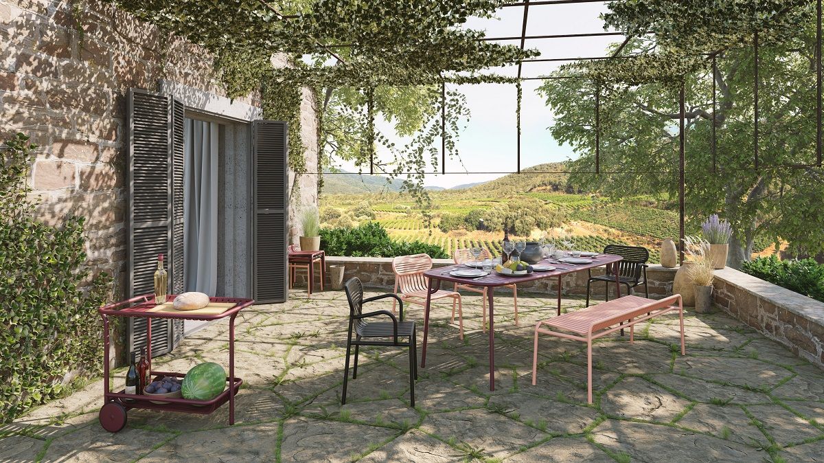 Terracottafarbener Week-End Stool Hocker von Petite Friture auf einer Terrasse mit Esstisch und Blick in die Landschaft.