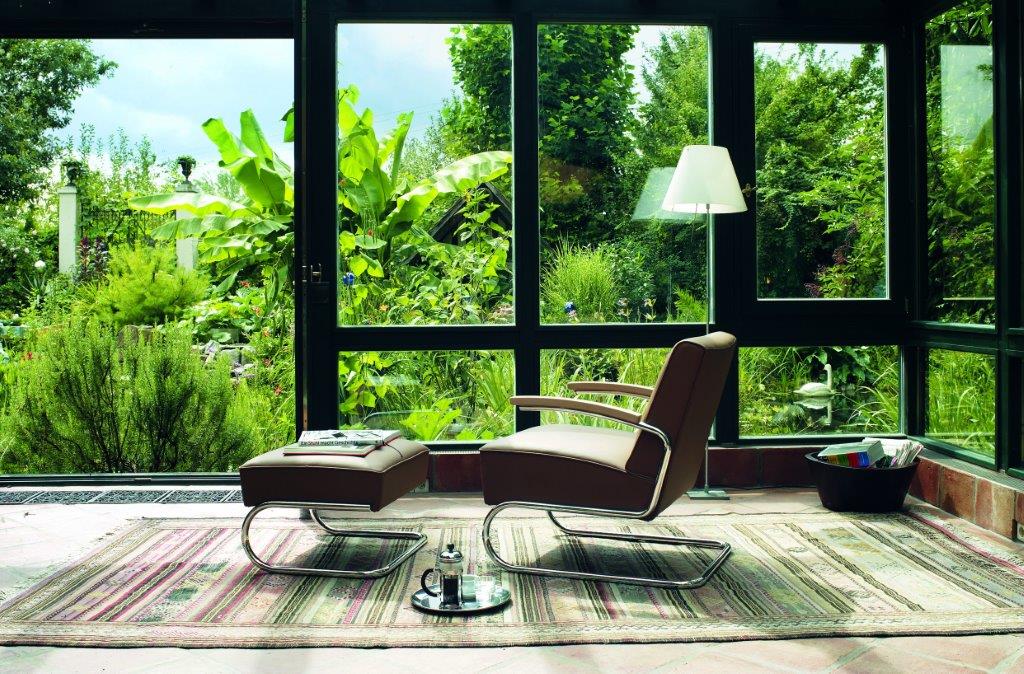 S 411 Freischwinger Sessel von Thonet mit braunem Lederbezug und passendem Hocker vor Fenster.