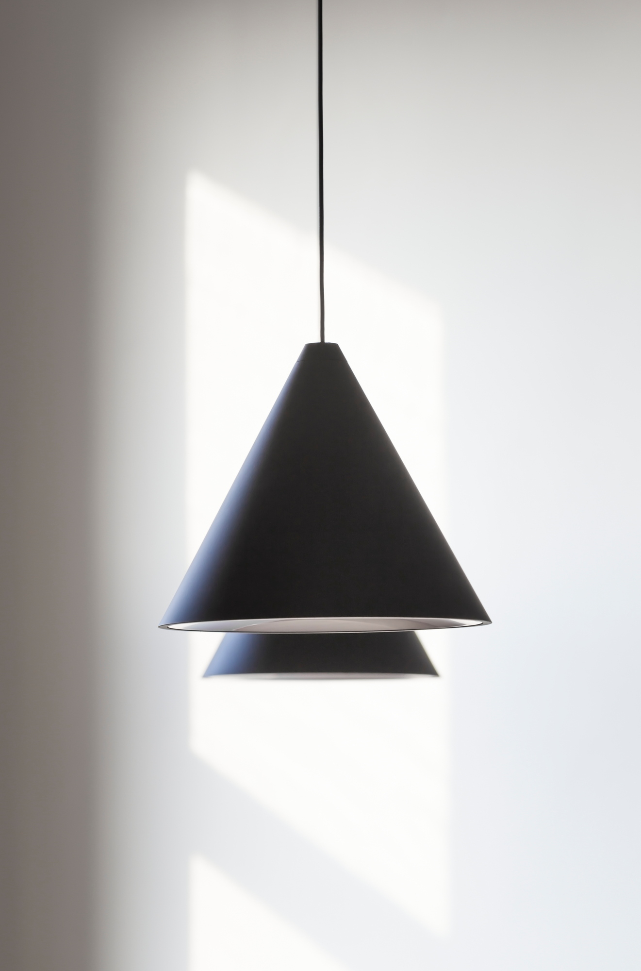 Schwarze Flos String Light Cone Head Pendelleuchte mit kegelförmigem Lampenschirm vor einer weißen Wand.