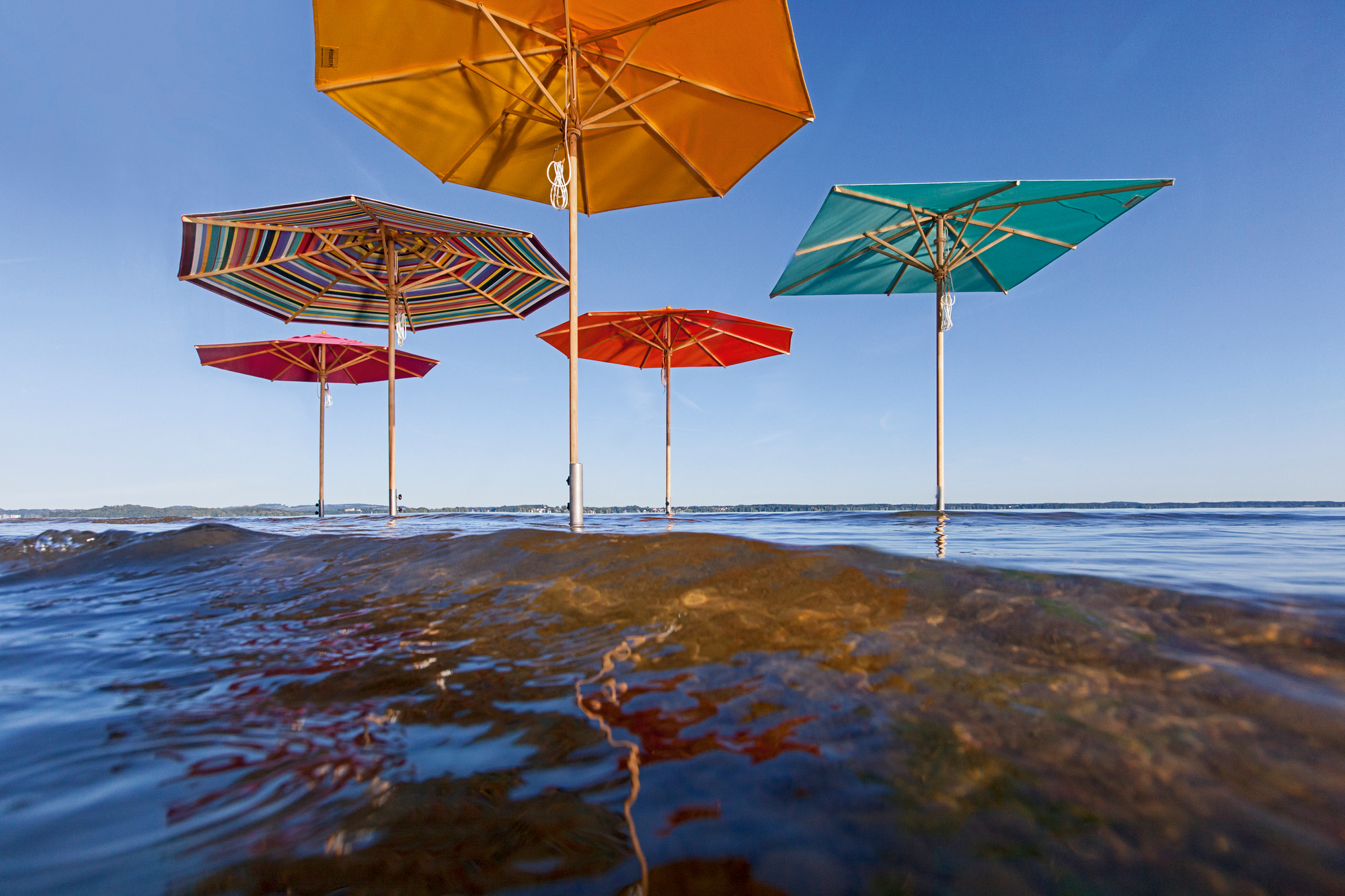 Mehrere bunte Sonnenschirme im Wasser, befestigt mit Bodenhülsen. Sonnenschutz und Schatten.
