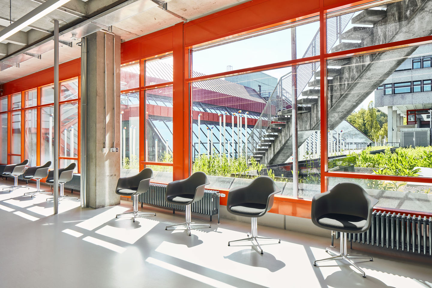 Innenaufnahme: Mehrere graue Eames Plastic Arm Chairs DAL mit Sitzpolster von Vitra in modernem Bürogebäude.