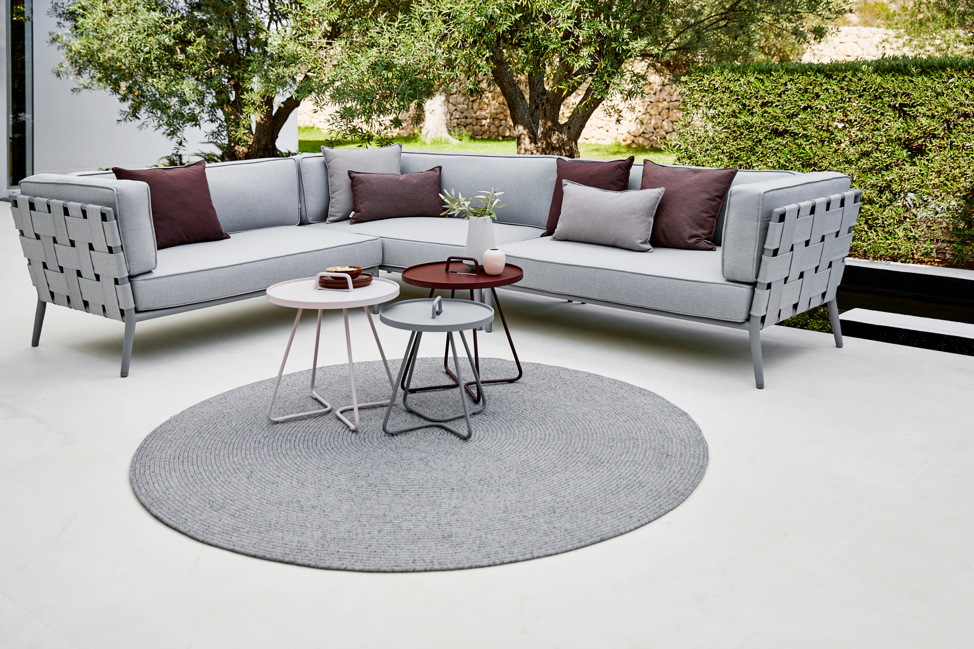Grauer Cane-Line Outdoor Beistelltisch, extra klein, auf einer Terrasse mit Lounge-Möbeln.