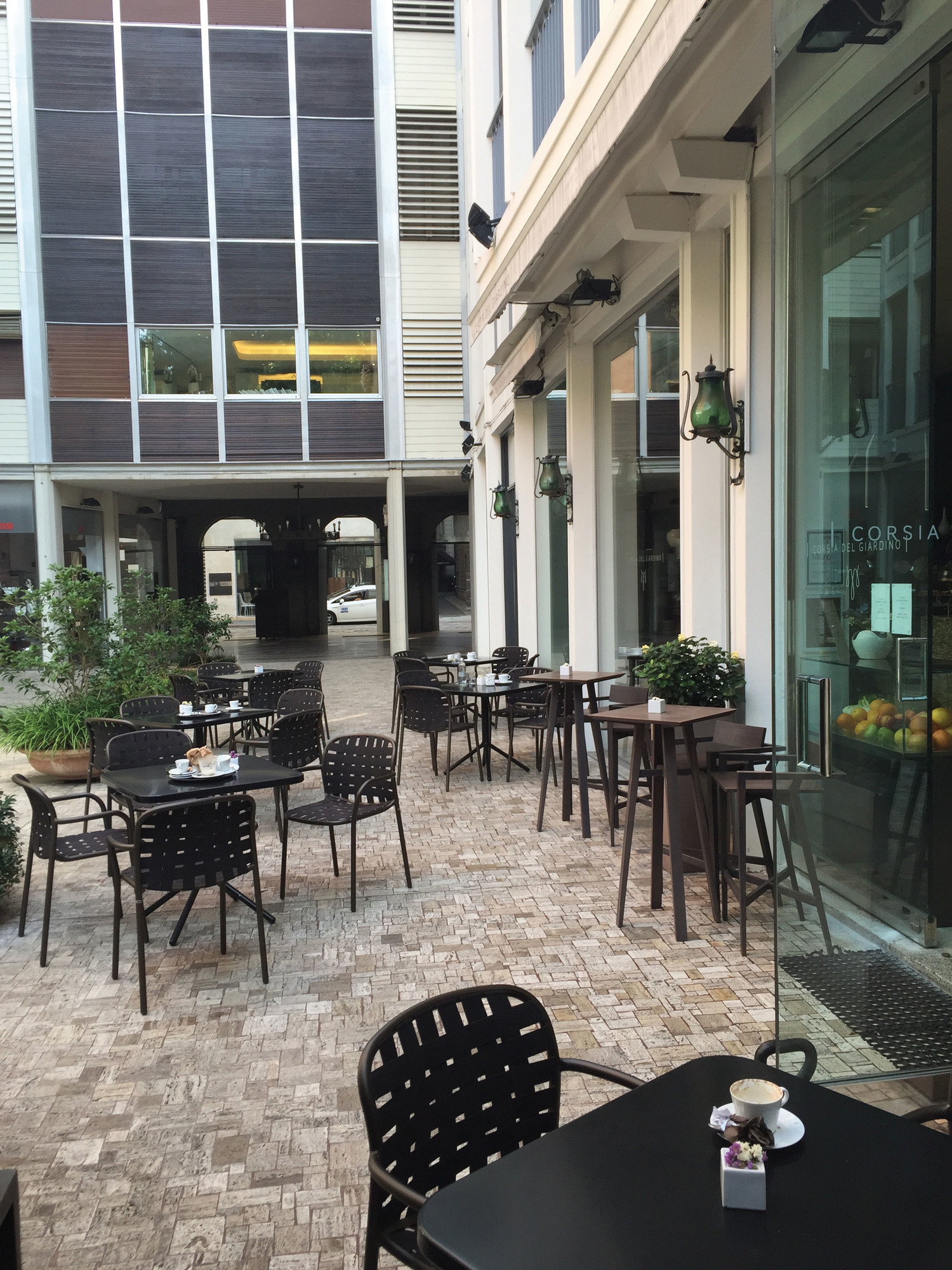 Außenbereich eines Cafés mit graugrünen Yard Armlehnstühlen und Tischen auf einem gepflasterten Platz.