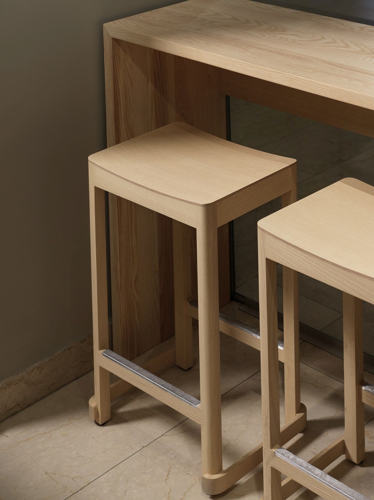 Detailaufnahme von zwei hellen Holz-Barhockern, Atelier Bar Stool von Artek, mit Fußstütze vor einem Bartisch.