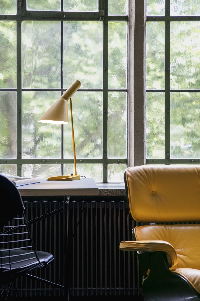 AJ Tischleuchte in Soft Lemon von Louis Poulsen auf einem Schreibtisch vor einem Fenster.
