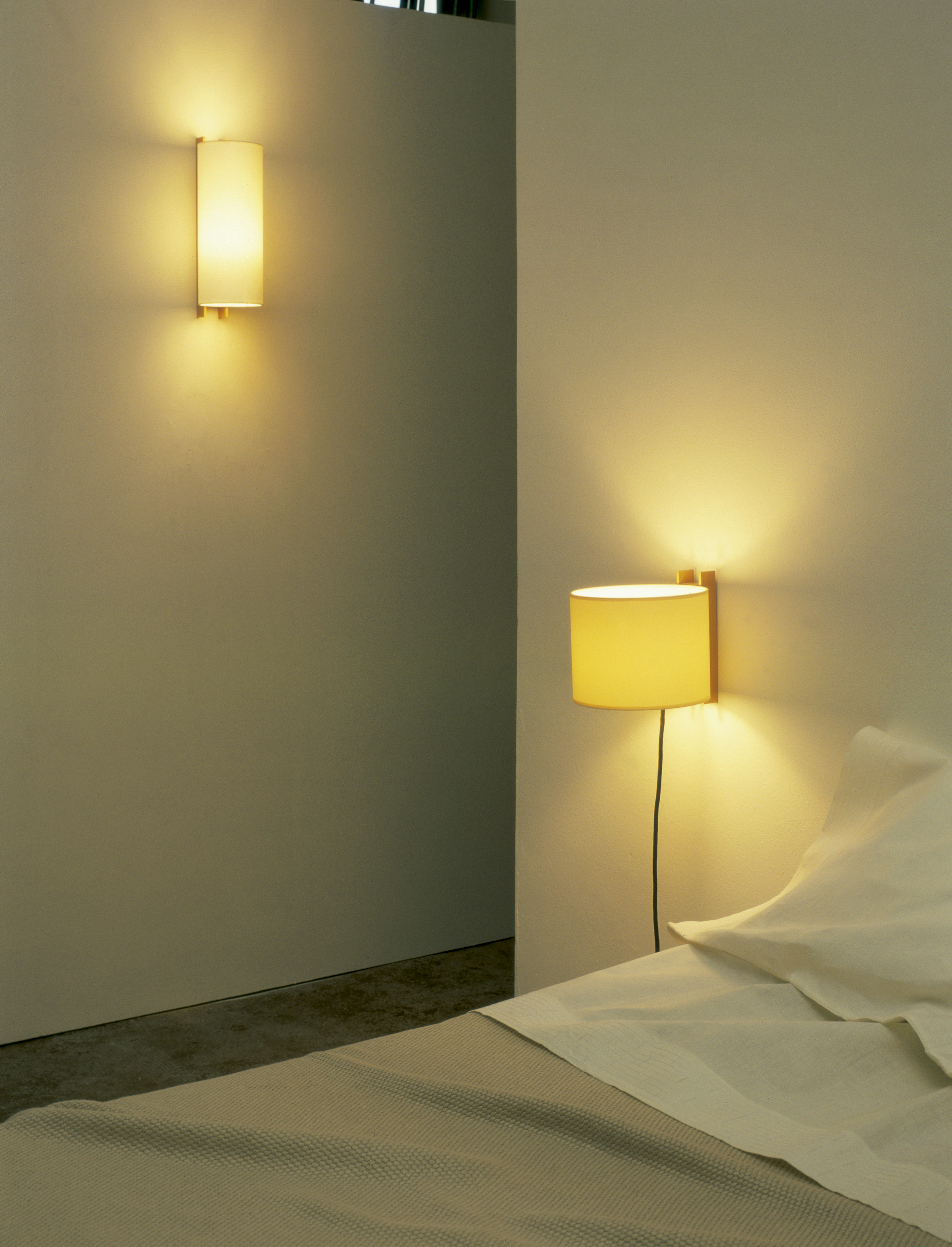 TMM largo Wandlampe von Santa & Cole neben einem Bett mit warmem Licht.