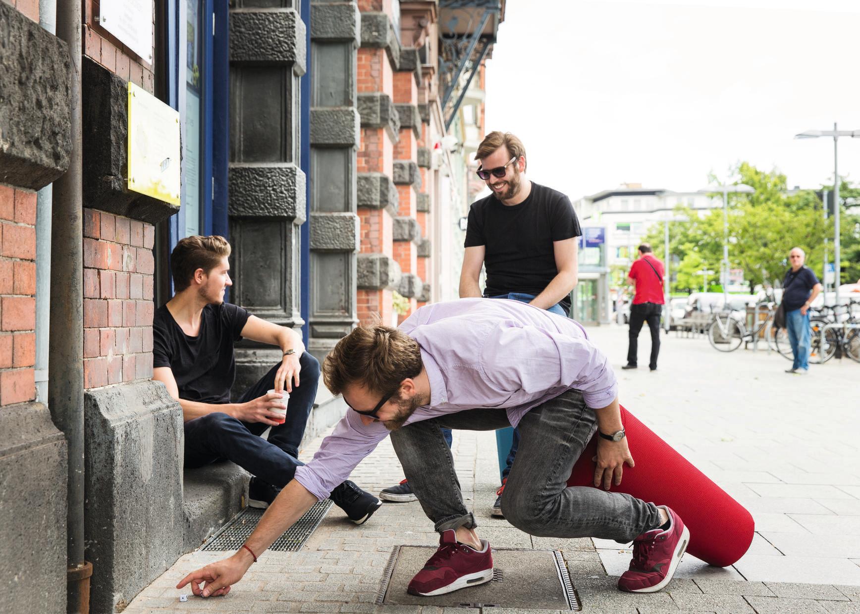 Mann hievt roten Wilkhahn Stand-Up Sitzhocker hoch, während andere Männer zusehen. Stehhilfe für ergonomisches Sitzen.