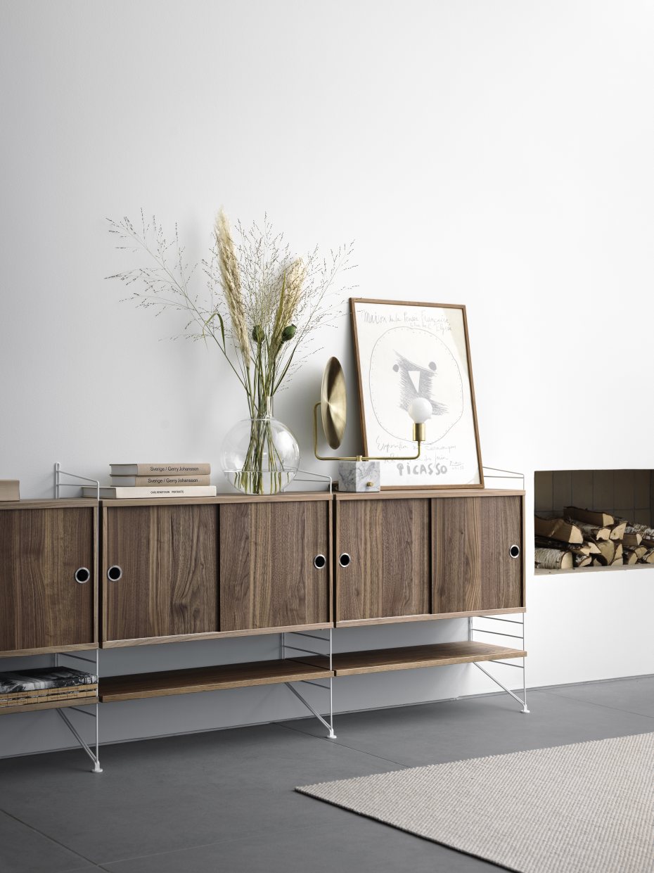 Wohnzimmer mit String Furniture Regalsystem in Holz und Weiß, dekoriert mit Vase und Kunst.