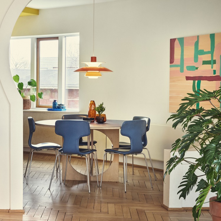 Esszimmer mit runden Holztisch und blauen Stühlen, darüber hängt eine orangefarbene PH 5 Pendelleuchte von Louis Poulsen.