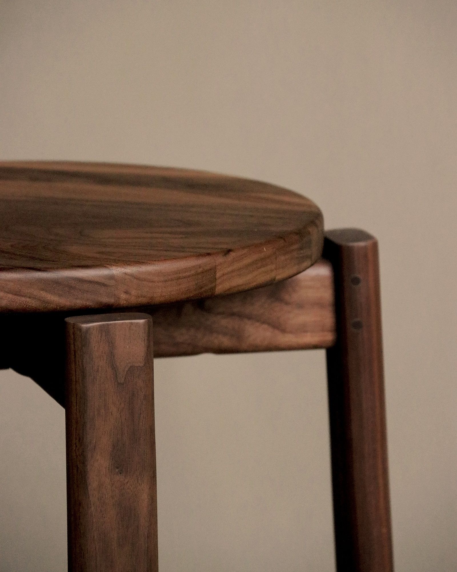 Detailaufnahme des Audo Copenhagen Passage Stool Hockers aus dunklem Holz mit runder Sitzfläche.