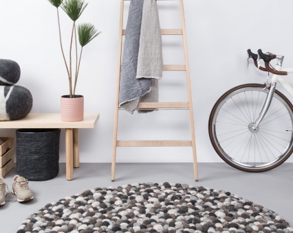 Runder Filzkugel Teppich in Grau- und Weißtönen im modernen Wohnraum mit Leiter und Fahrrad.